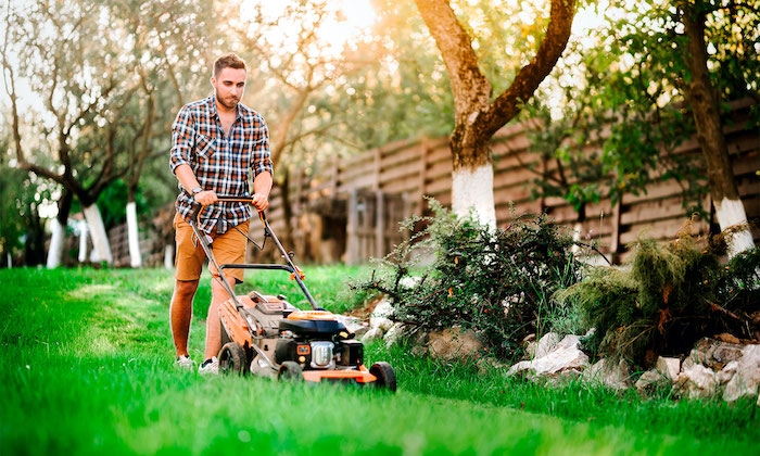 un homme équipée d une tondeuse tond la pelouse dans le jardin