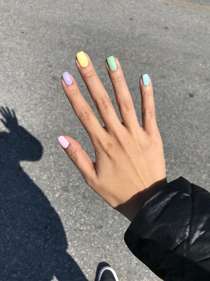 un main avec des ongles teints en couleurs pastels diffférentes