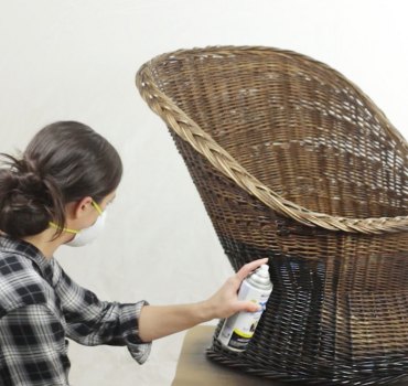 une femme avec masque peint une chaise en rotin avec de la peinture en aérosole