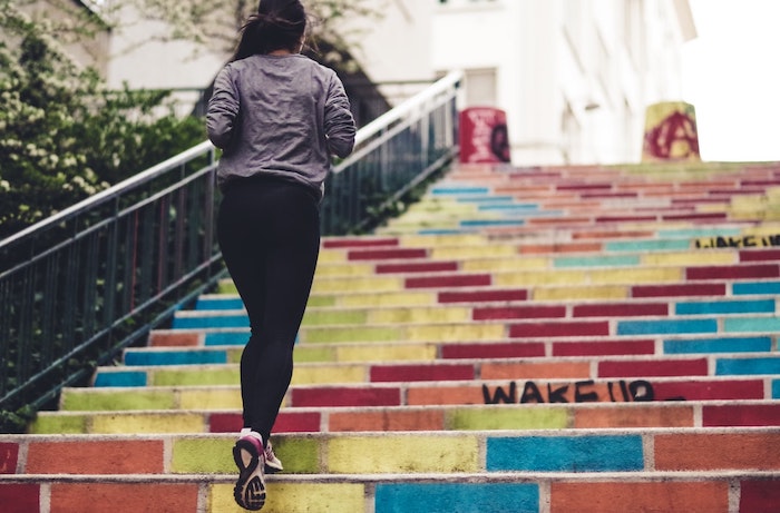 une femme en pantalon noir monte des escaliers multicolores dans la ville