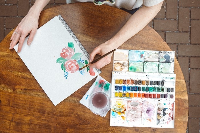 une fille qui dessine des fleurs a l aquqrelle sur un feuille de papier table en bois ronde