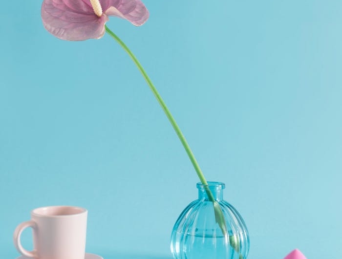 une fleure dans une vase ronde a coté d une tasse a cafe et une eponge a maquillage
