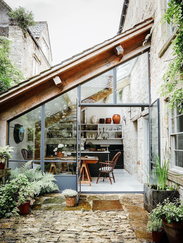 une véranda a coté de maison protégé par une toiture en verre et entourée des plantes vertes