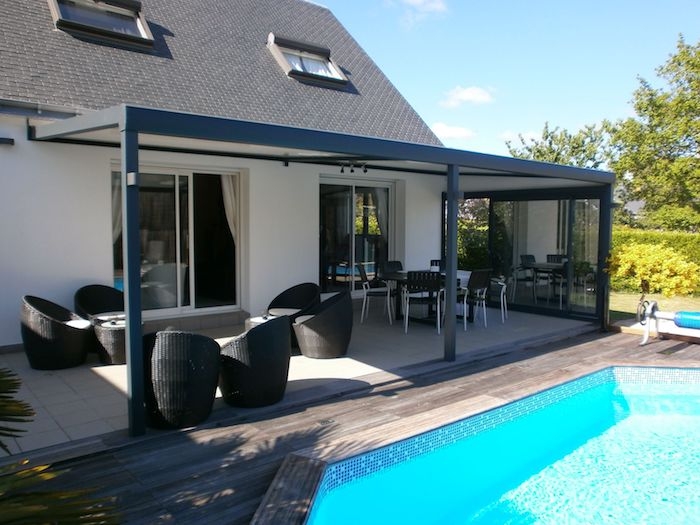 veranda bioclimatique devant une maison avec piscine et meubles en rotin