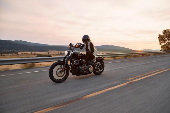 moto noir harley davidson femme blonde sur le moto vue vers la montagne chmps de ble