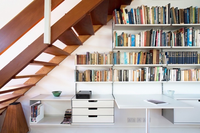 bibliothèque sous escalier en bois livres et magazines bureau et murs blancs