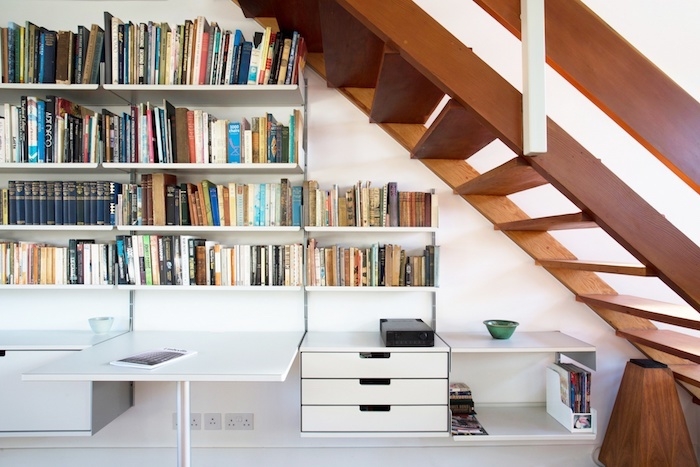 bibliothèque sous escalier en bois livres et magazines bureau et murs blancs