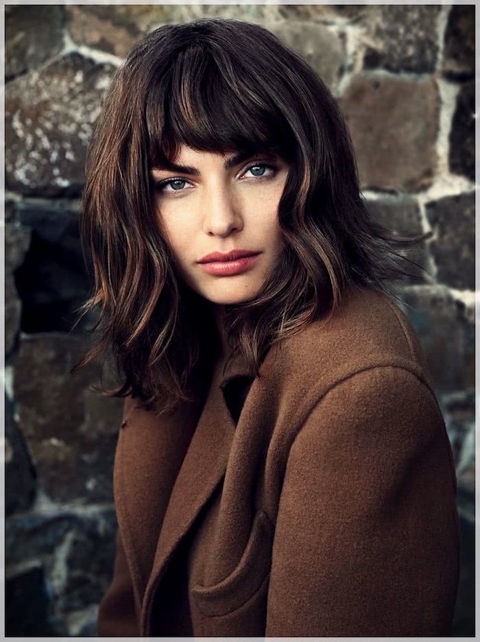 décoiffée coupe courte femme 2021 tendance brune au manteau marron devant un mur de tuiles