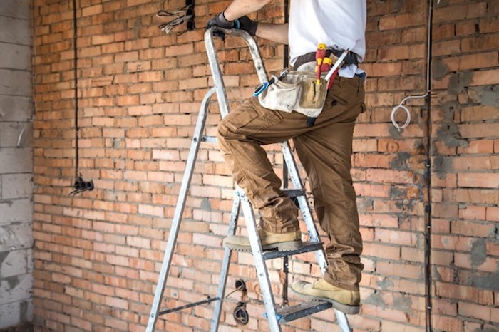 electricien pantalon beige pour homme avec оutiles mur en brique