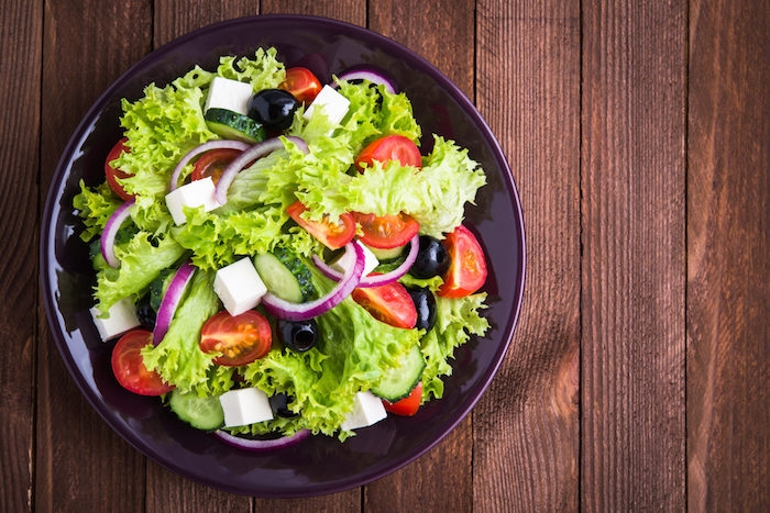 greek salad (lettuce, tomatoes, feta cheese, cucumbers, black olives, purple onion) on dark wooden background top view. healthy food. space for text.