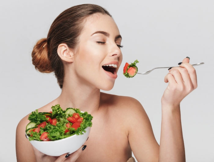 young woman eating healthy salad isolated on white