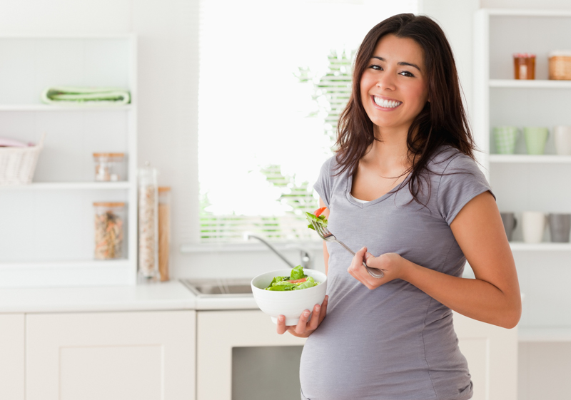 attractive pregnant woman holding a bowl of salad while standing