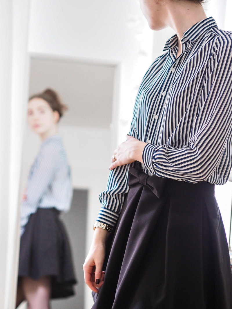 style classe femme une chemise noire et blanche rentrée dans une jupe dans le miroir