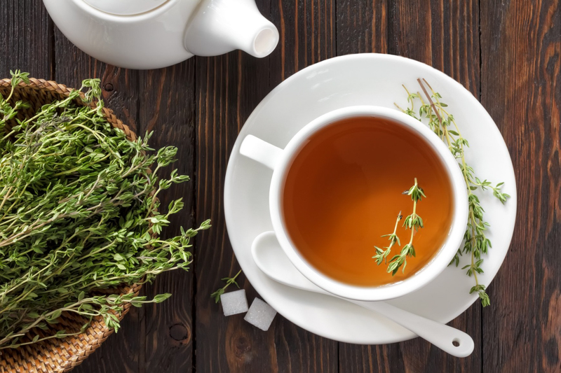 erbe aromatiche che cucinano il tè al timo in una piccola tazza bianca