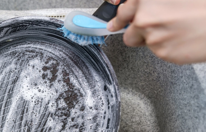 woman launches a burnt pan with a blue brush in the kitchen sink