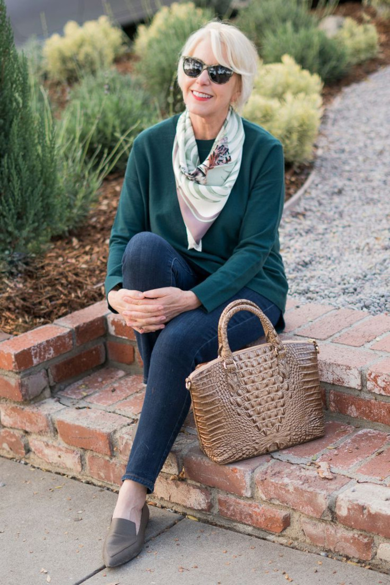 elegant dressed woman in dark green sweater blue jeans loafers scarf and sunglasses