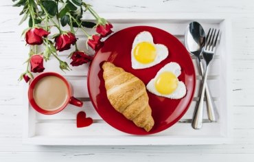 bouquet de roses rouges meilleur petit déjeuner assiette ronde rouge croissants oeufs en coeur