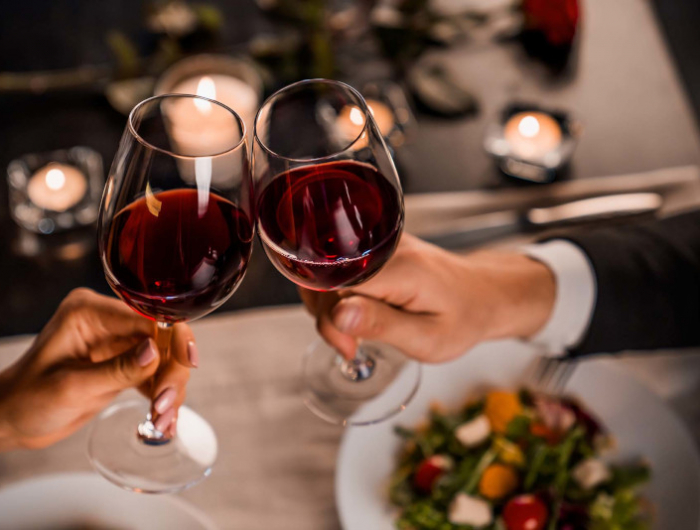 close up of young couple toasting with glasses of red wine at restaurant