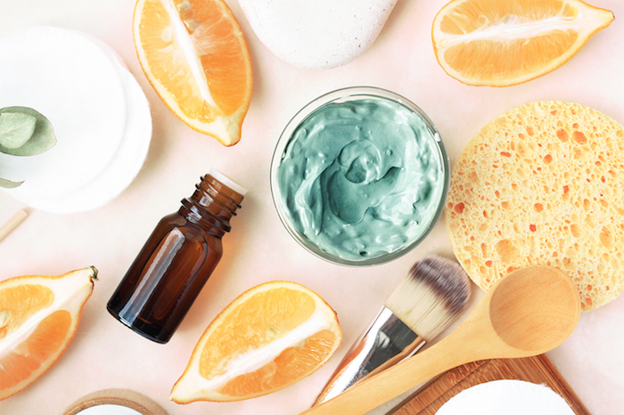 des oranges coupés sur une surface rose avec des brosses une bouteille d huile essetiel et une mixture bleue