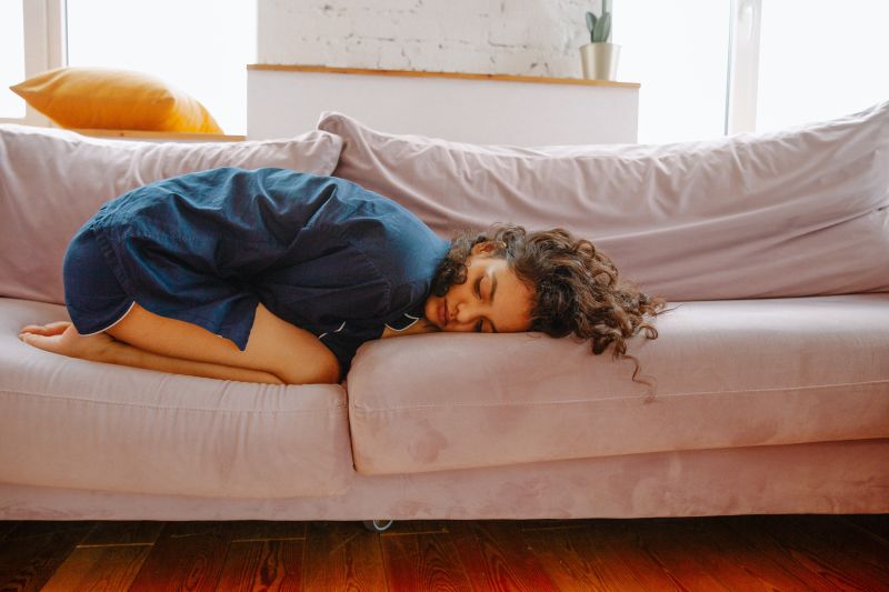 douleur regle une fille blottie sur un canapé à cause du mal au ventre