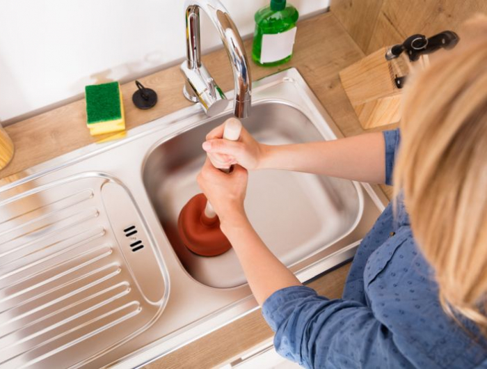 high angle view of woman using plunger in blocked kitchen sink to unclog drain