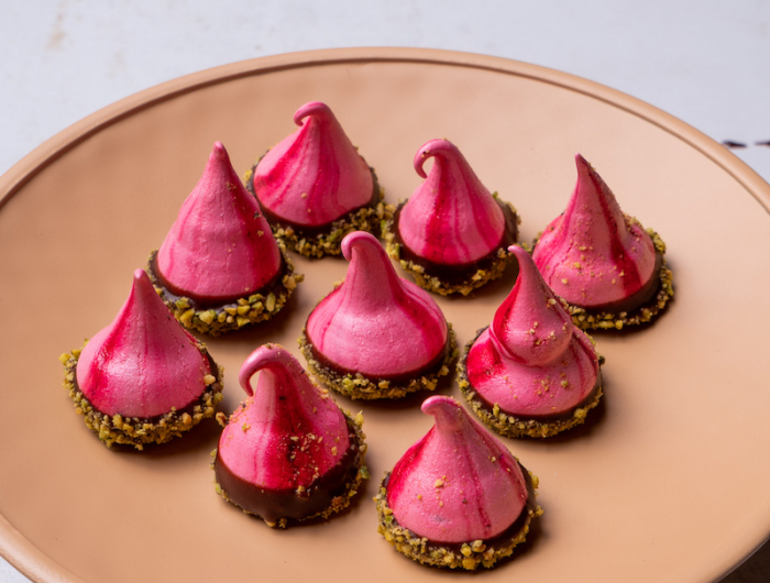 meringue forme originale de couleur rose au chocolat et pistaches rangées dans une assiette