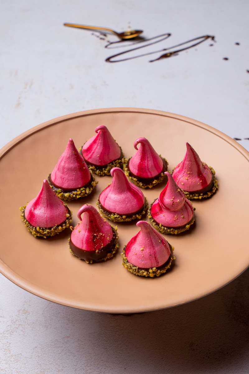 meringue forme originale de couleur rose au chocolat et pistaches rangées dans une assiette