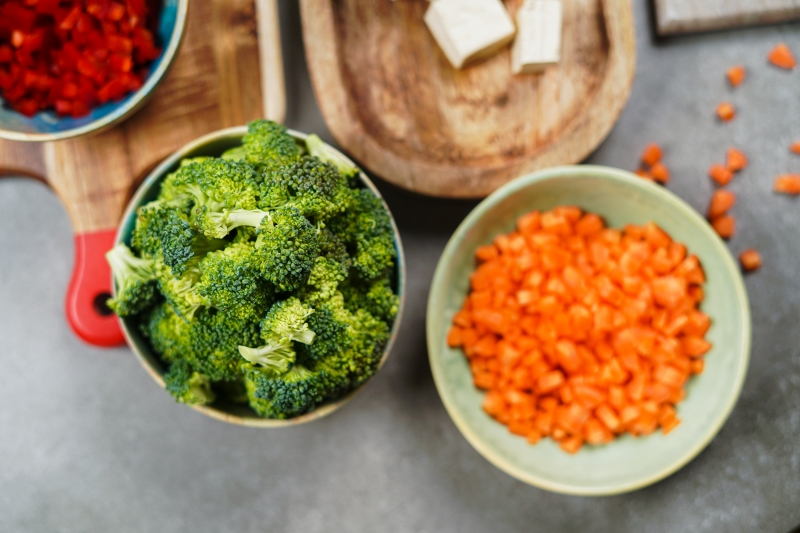 bol vert brocoli carottes coupes en des planche a couper bois poivron rouge