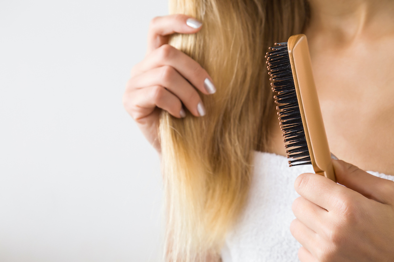 woman's hand brushing blonde hair. cares about a healthy and clean hair. beauty salon. empty place for a text on the gray background.