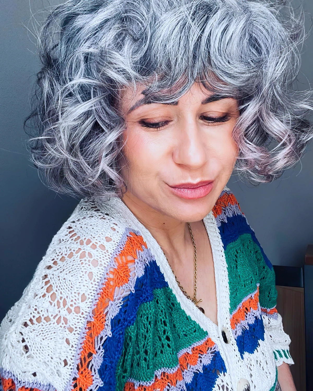 femme avec cheveux gris boucles portant un cardinagn colore illustrant une coiffure naturelle et soignee