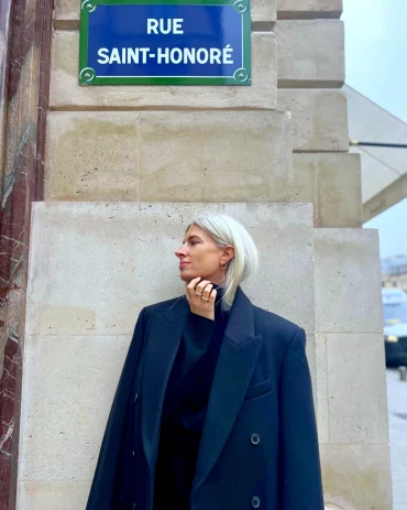 femme elegante avec cheveux blancs courts posant devant un panneau de rue saint honore
