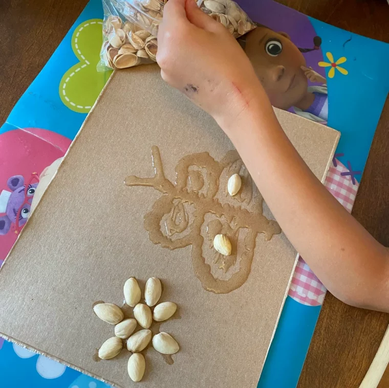 un enfant qui colle des coquilles de pistache sur un carton