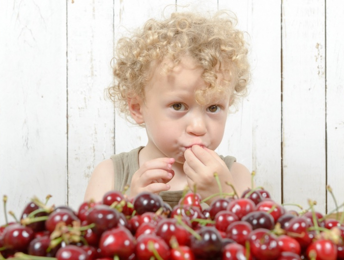 a small blond boy eating cherries