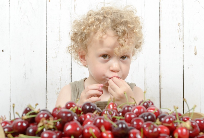 a small blond boy eating cherries