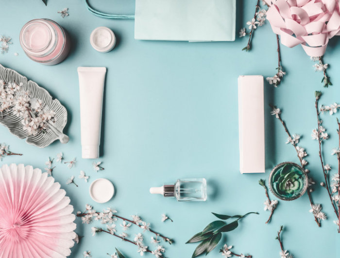 beauty concept with facial cosmetic products, shopping bag and twigs with cherry blossom on pastel blue desktop background. modern spring skin care trends, top view, frame, flat lay. branding mock up