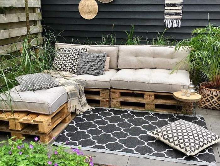 meuble de jardin avec palette en bois sur une terrasse avec des coussin graphyaue et plantes vertes