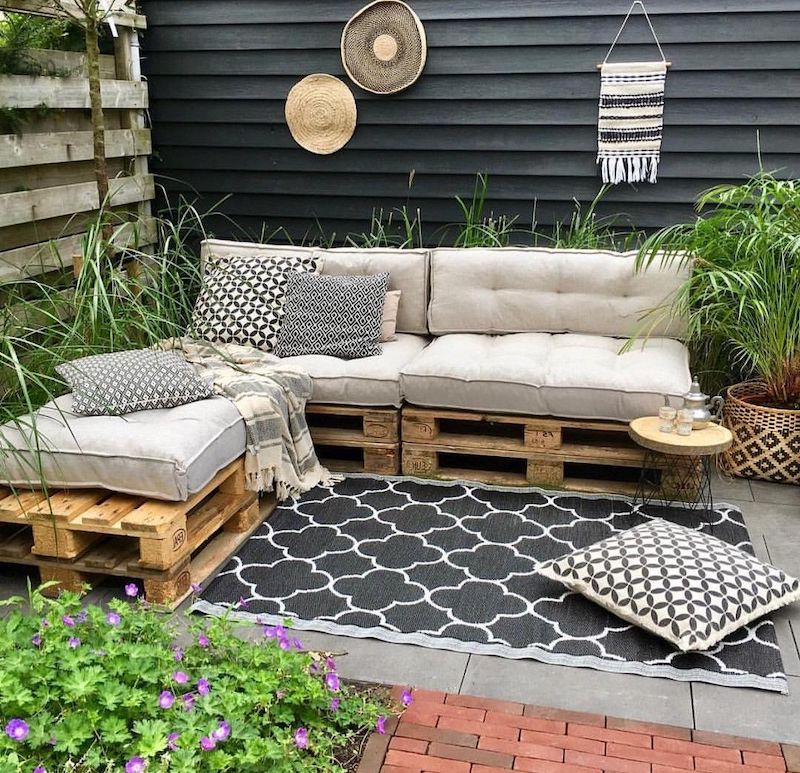 meuble de jardin avec palette en bois sur une terrasse avec des coussin graphyaue et plantes vertes