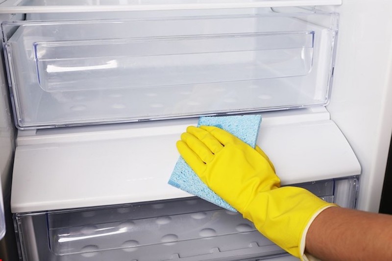 nettoyer le frigo avec du vinaigre blanc une main en gang jaune essuie les etagers