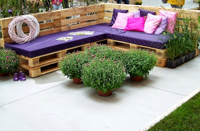 salon de jardin en palette de bois grand canape en bois avec coussins violettes et des fleurs autour