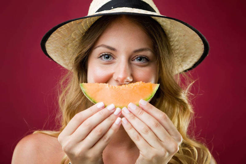 melon calorie regime une femme tenat un melon devant la bouche avec un chapeau