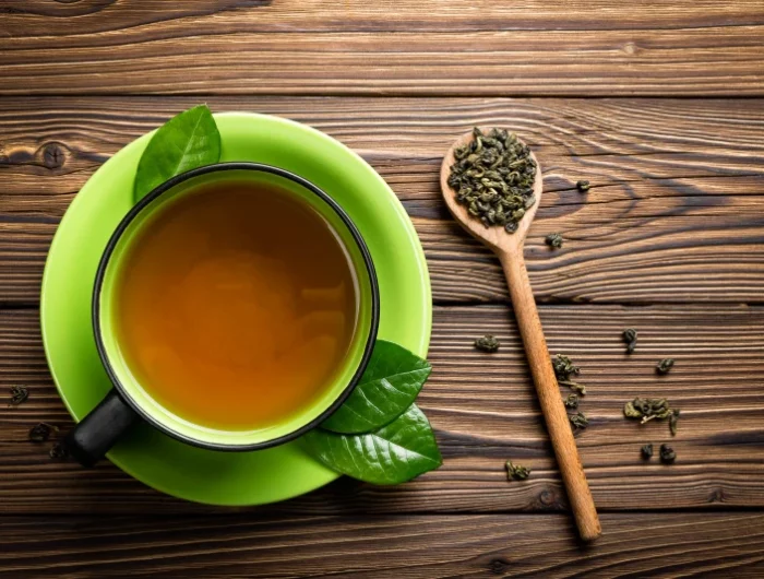 une tasse de thé vert sur une table en bois une cuillère en bois remplie de the