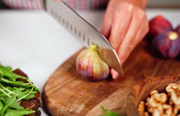 une main qui coupe une figue en deux salade verte couteau