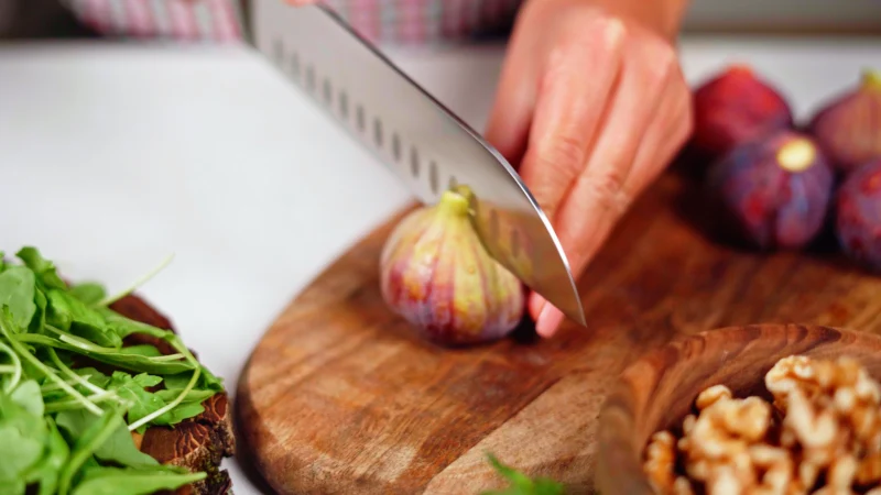 A hand cut a fig in half with a green salad knife