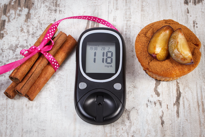 glucometer, plum muffins and cinnamon sticks on wooden background, diabetes and delicious dessert