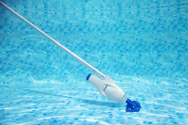 aspirateur manuel au fond de la piscine avec des motifs de mosaique bleue