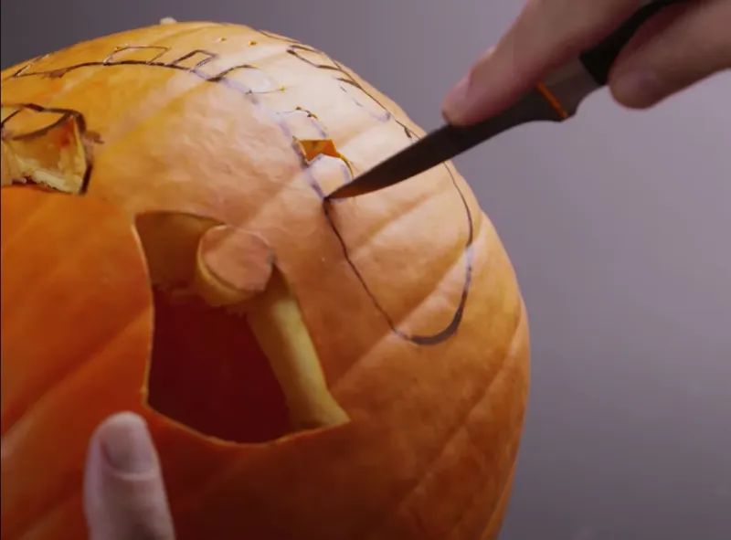 couteau qui decoupe une citrouille orange avec des trous sur sa surface