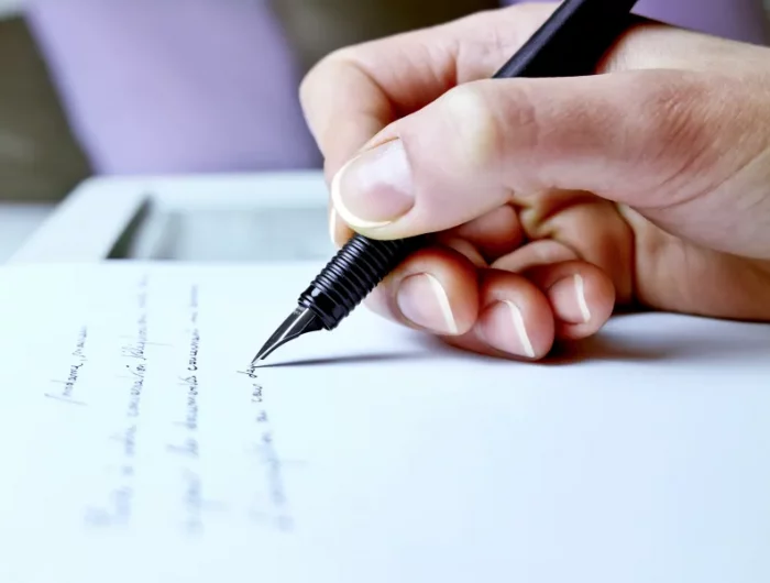 main qui ecrit avec un stylo a encre sur une feuille blanche