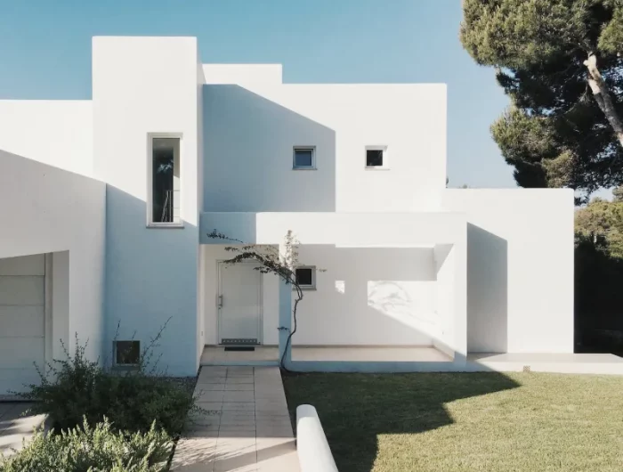 maison en beton blanc pelouse et arbuste devant la maison