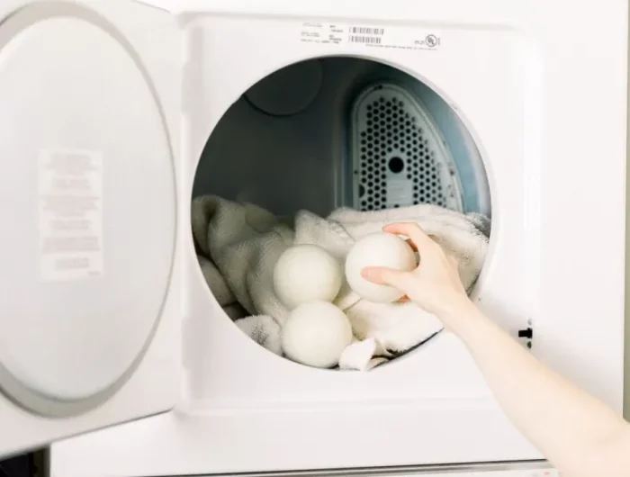 un bras mettant des balles en laine dans un seche linge blanc avec des serviettes