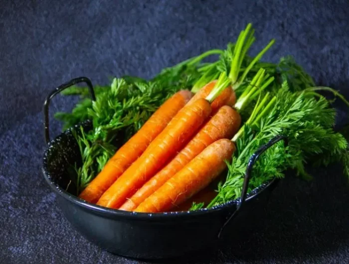 carottes separees sur un lit de fanes dans un recipent bleu sur fond bleu